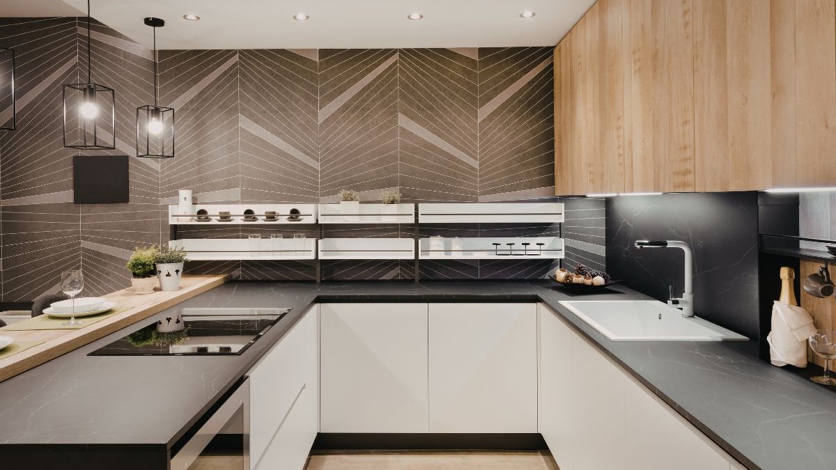 Cozinha moderna em U com bancadas escuras, arm&aacute;rios brancos e amadeirados, pia e fog&atilde;o de indu&ccedil;&atilde;o integrados.