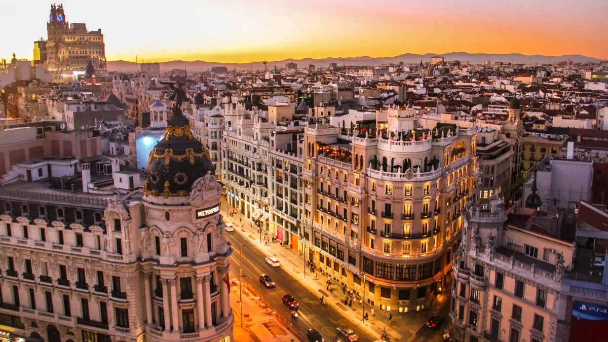 Madri ao entardecer: a vibrante capital espanhola oferece a jogadores de futebol a combinação perfeita de vida cultural e excelência esportiva. Vista aérea da Gran Vía em Madri ao entardecer, com o Edifício Metrópolis e rua movimentada.