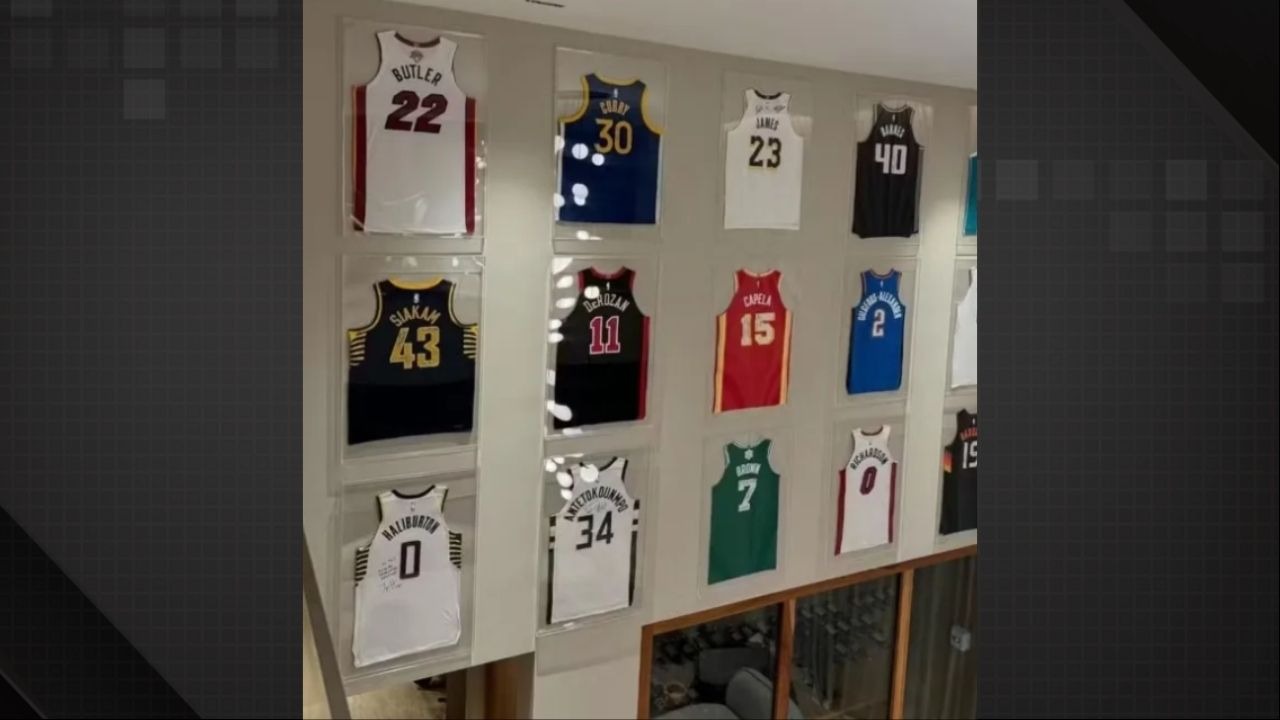 O interior da mansão de Vini Jr. exibe uma coleção de camisas de basquete emolduradas, destacando a área de lazer do imóvel - Foto: Reprodução/Redes Sociais Parede com doze camisas de basquete emolduradas, incluindo Butler 22, Curry 30 e James 23