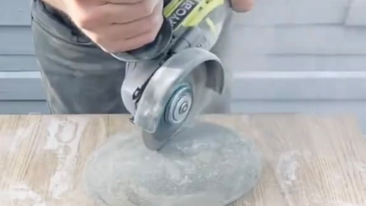O processo de fabricação de tigelas de pedra começa com o corte da base utilizando uma esmerilhadeira Mão segura esmerilhadeira Ryobi cortando uma pedra redonda sobre madeira, gerando poeira