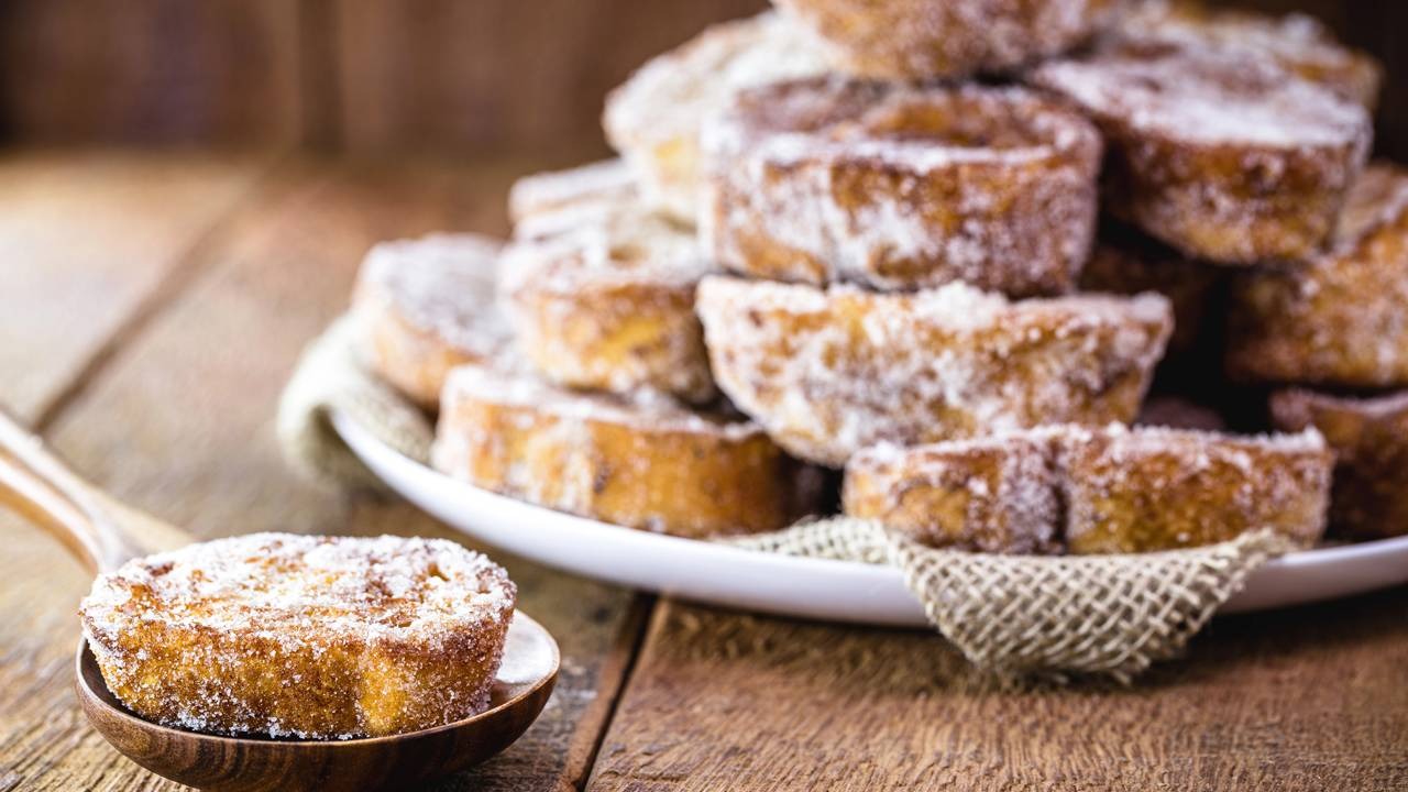 A rabanada com sua casquinha crocante e miolo macio. Rabanadas douradas com açúcar e canela em prato branco e colher de madeira sobre mesa rústica