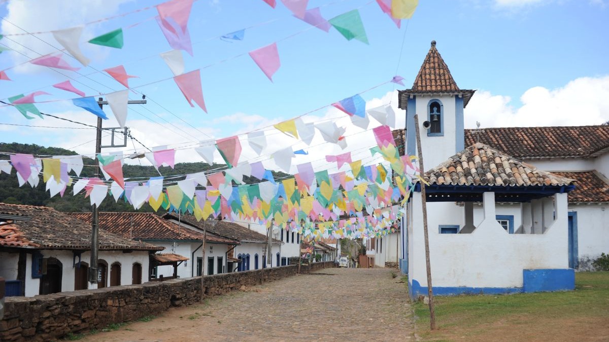 Rua de paralelep&iacute;pedos decorada com bandeirinhas coloridas, casas coloniais e igreja com torre.