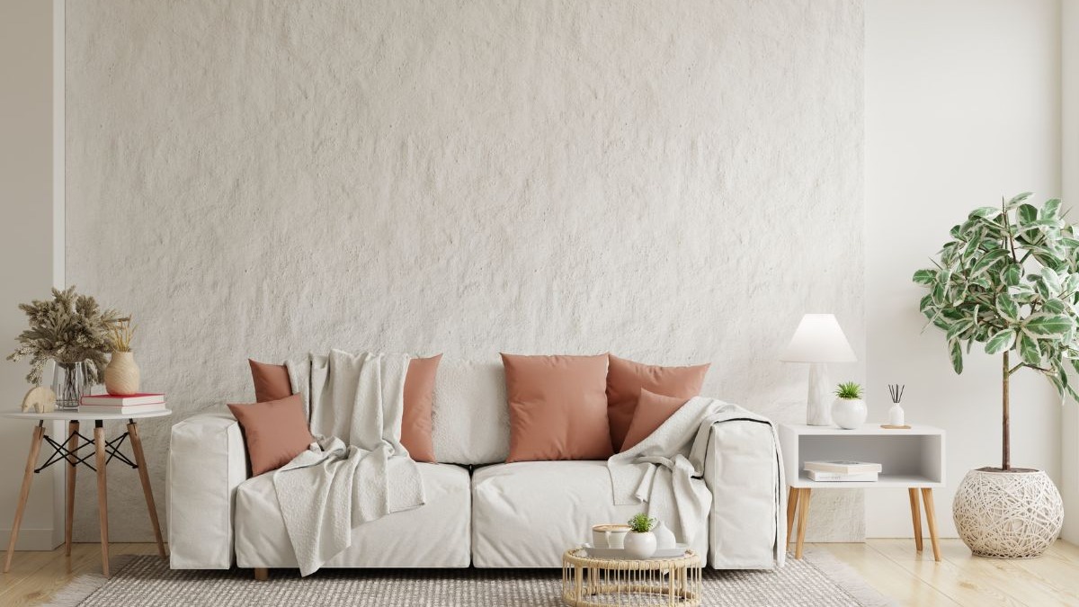 Sala de estar clara com sof&aacute; branco, almofadas terracota, mesa lateral e planta em vaso.