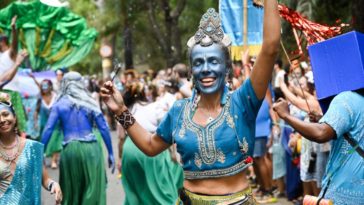 Mulher sorridente com rosto e corpo pintados de azul e cocar em bloco de carnaval.