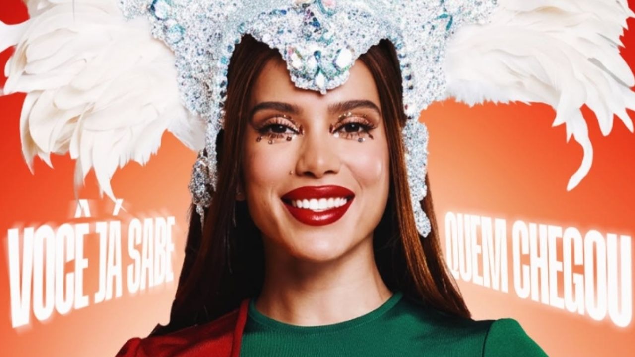 Anitta celebra seu anúncio como nova Rainha de Bateria da Grande Rio. Cantora Anitta sorri com cocar carnavalesco brilhante, penas, maquiagem glitter e batom vermelho forte