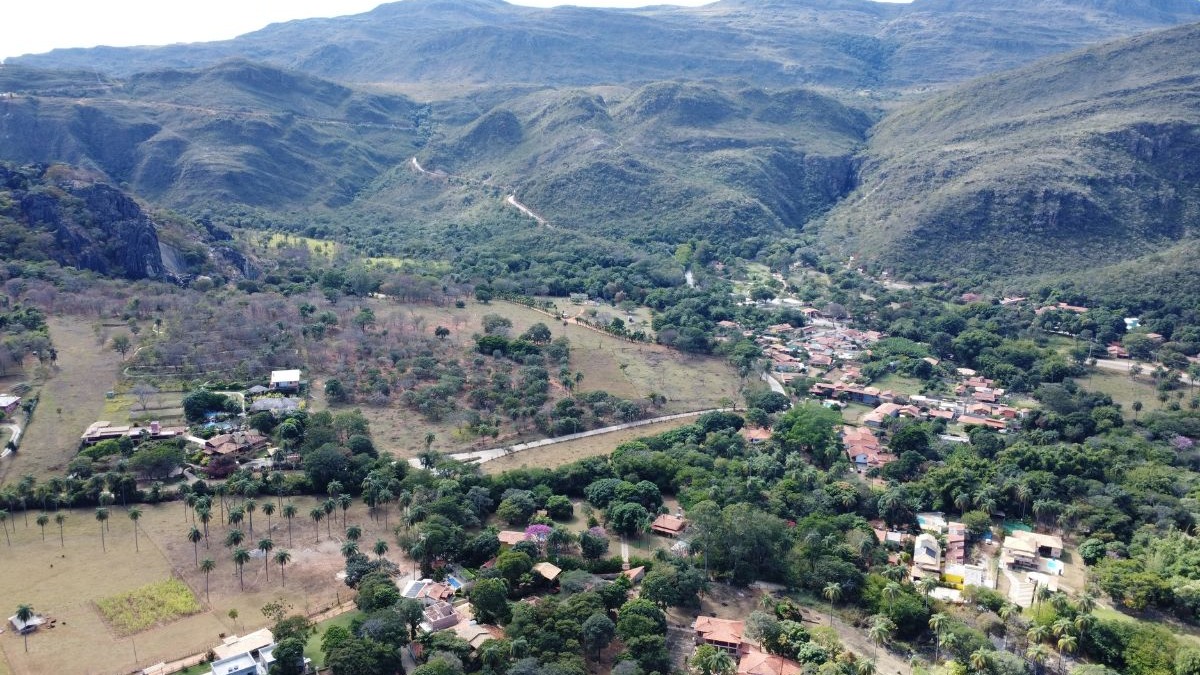 Vista a&eacute;rea de vale montanhoso com vilarejo, &aacute;rvores verdes, vegeta&ccedil;&atilde;o seca e estradas.