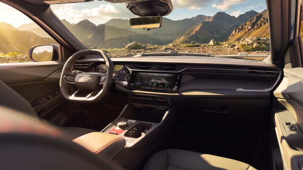 Interior do Jeep Cherokee Trailhawk com volante, painel, tela multim&iacute;dia e montanhas ao fundo