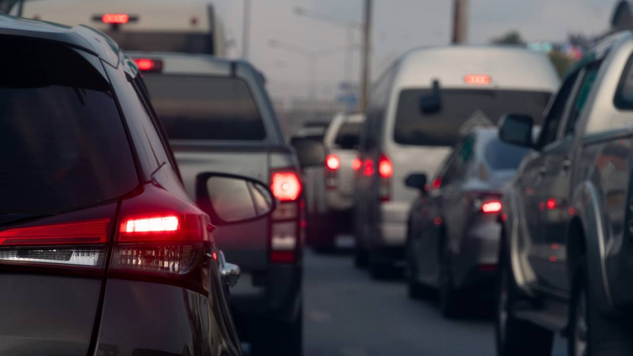 Evitar o fluxo intenso de veículos é essencial para quem planeja viajar no feriado de Corpus Christi, conforme orienta a matéria. Trânsito intenso com vários carros parados na estrada, luzes traseiras acesas.