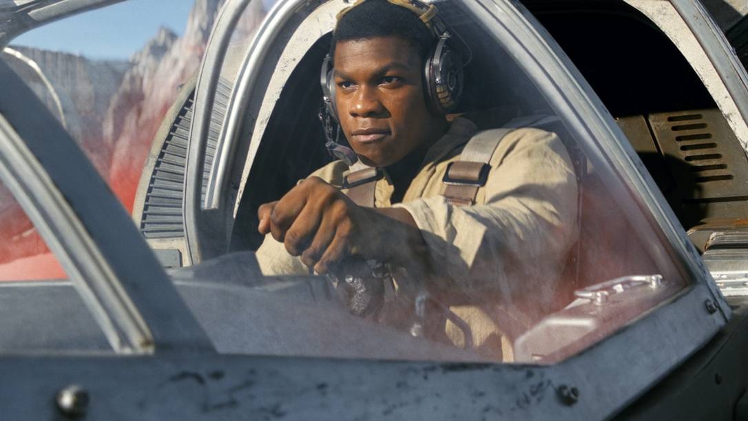 O ator John Boyega, que quase viu o roteiro de Star Wars vazar após um descuido com o documento. Ator John Boyega em cockpit, fone de ouvido, uniforme bege, mãos no controle