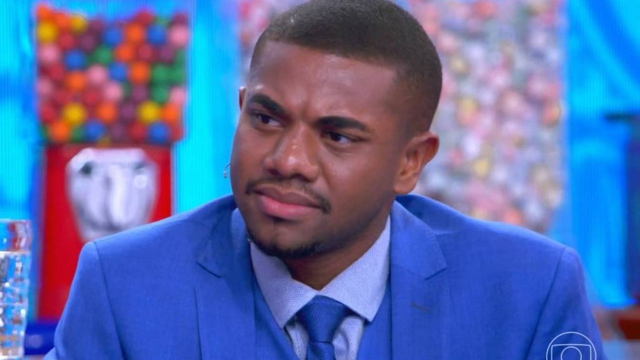 Jovem em destaque que representa o universo do Big Brother Brasil e suas complexidades. Foto: Reprodução/TV Globo Homem negro de terno azul com expressão séria em ambiente de estúdio, fundo colorido.