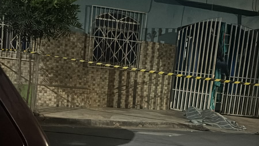 Cena do feminicídio que vitimou Adriana Gonçalves na residência em Arcos, Minas Gerais. - Foto: Reprodução Fachada de casa noturna com fita de isolamento amarela e preta e corpo coberto na calçada