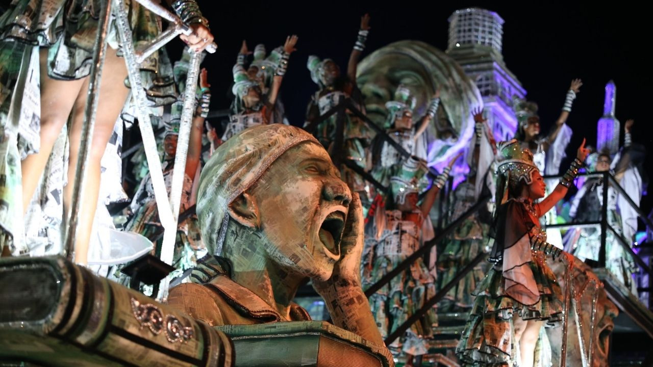 Escultura de cabe&ccedil;a gritando feita de jornal em carro aleg&oacute;rico de escola de samba &agrave; noite.