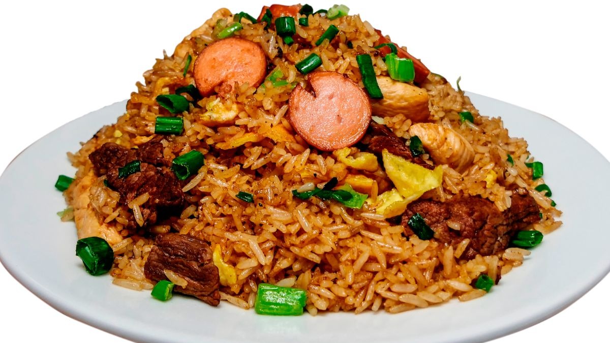 Sabores marcantes e ingredientes variados compõem a rica identidade gastronômica brasileira, destacada na matéria. Prato cheio de arroz frito com carne bovina, frango, ovos, salsicha e cebolinha picada.