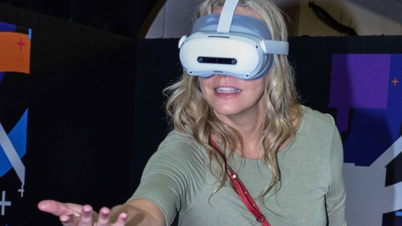 Mulher loira usa &oacute;culos de realidade virtual PICO 4 Ultra Enterprise com a m&atilde;o estendida.