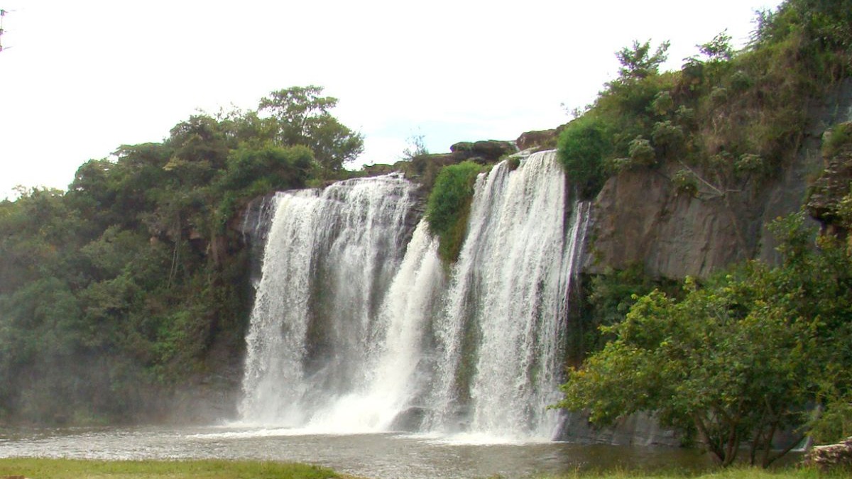 Cachoeira volumosa com m&uacute;ltiplos jatos d'&aacute;gua caindo sobre rochas e vegeta&ccedil;&atilde;o densa.