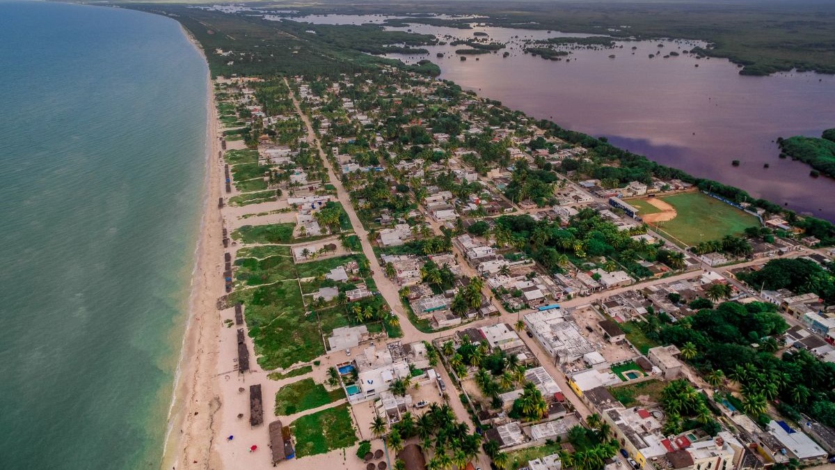Vista a&eacute;rea de cidade costeira mexicana com praia, oceano, casas, palmeiras e lagoa.