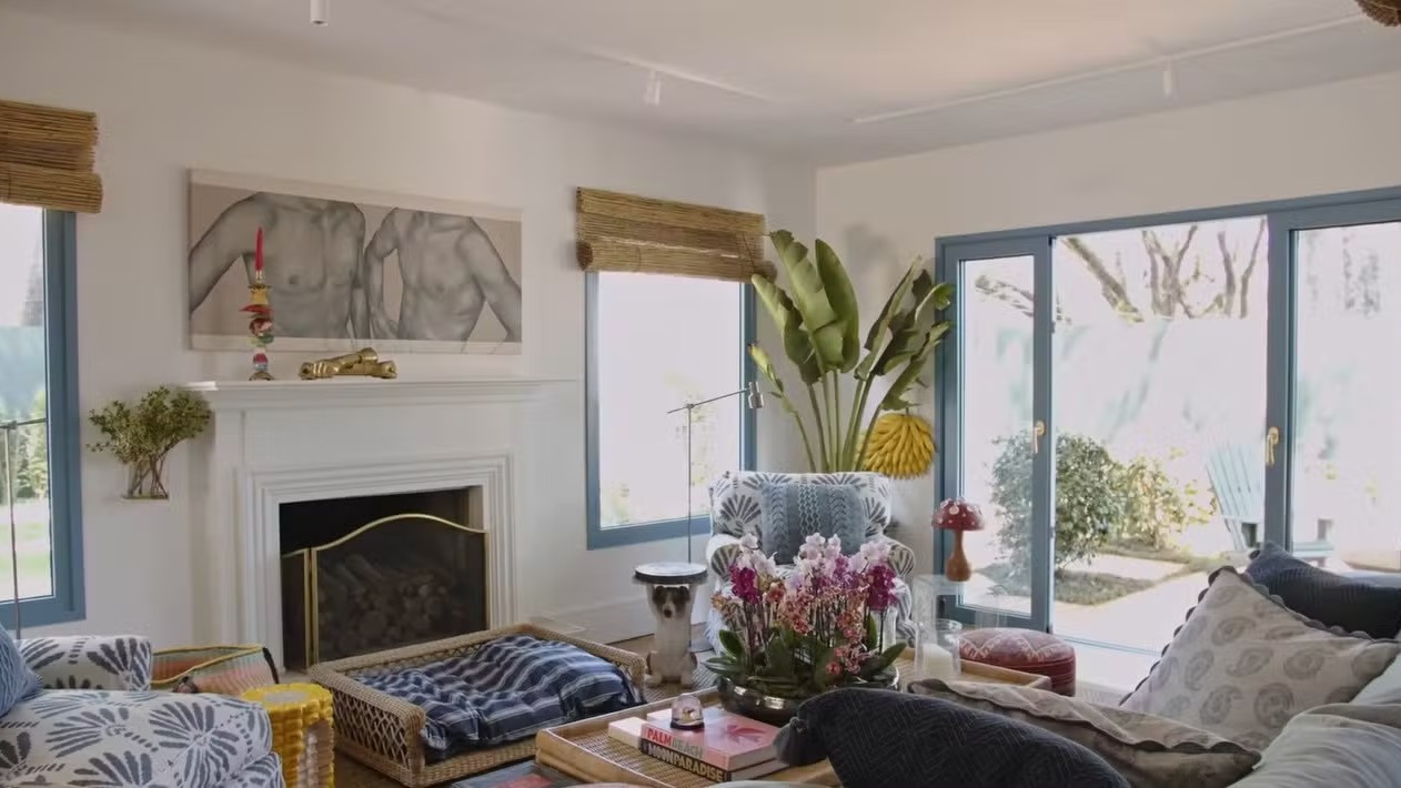 Sala de estar com lareira branca, quadro de torsos, janelas grandes e plantas variadas
