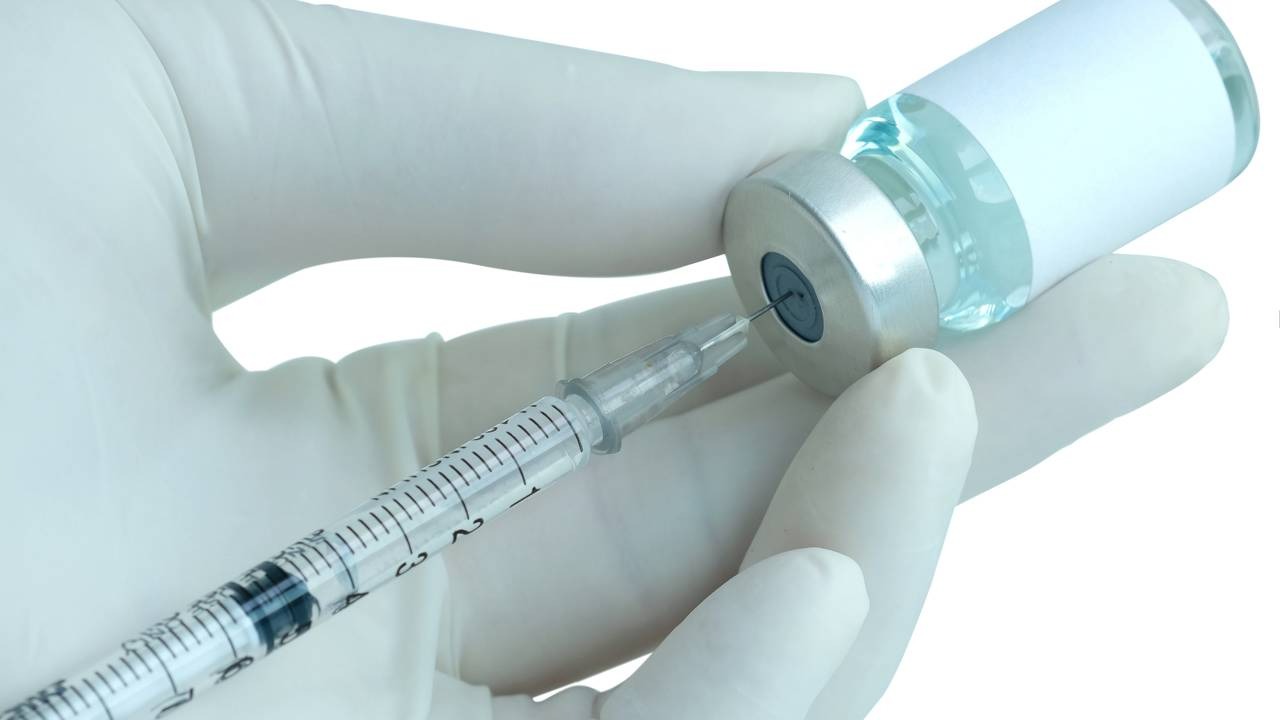Preparação de imunizantes para a Campanha de Multivacinação no Rio de Janeiro. Mão com luva médica inserindo seringa em frasco de vacina com líquido azul