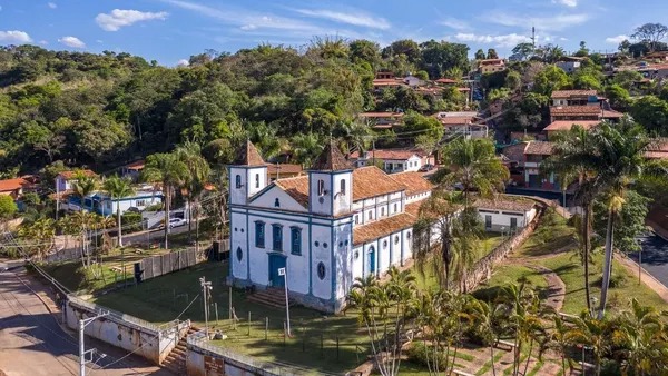 Igreja colonial branca e azul com duas torres em cidade histórica, cercada por casas e árvores.