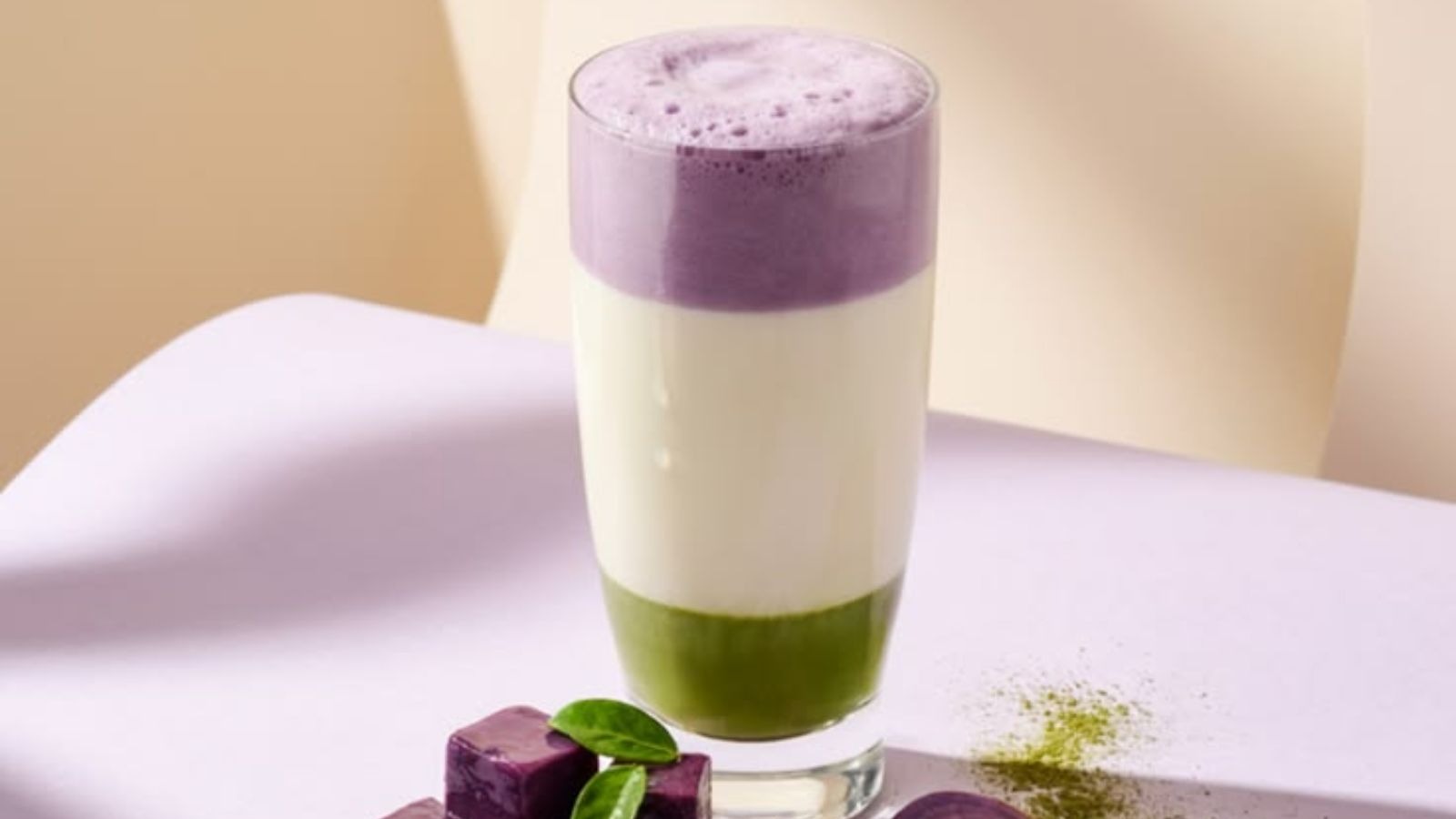 Bebida em camadas: verde, branco, roxo espumoso em copo, com cubos roxos e p&oacute; verde