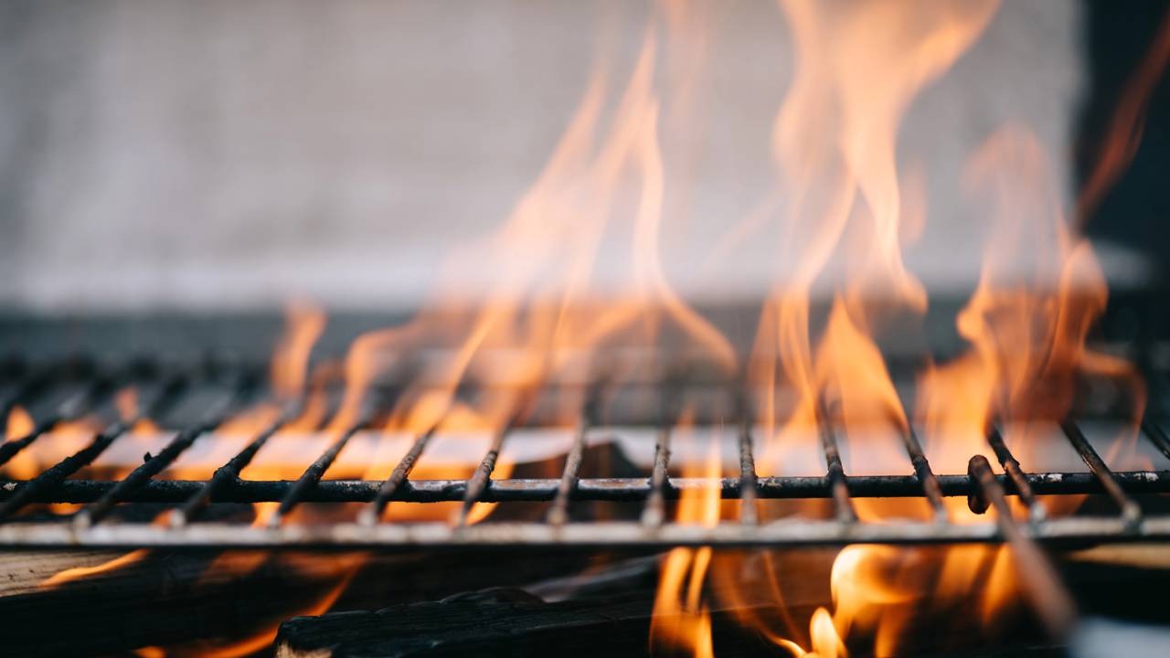 O fogo intenso é essencial para selar a carne e realçar o sabor, garantindo um churrasco perfeito. Churrasqueira com grelha metálica sobre chamas de fogo intenso e brilhante