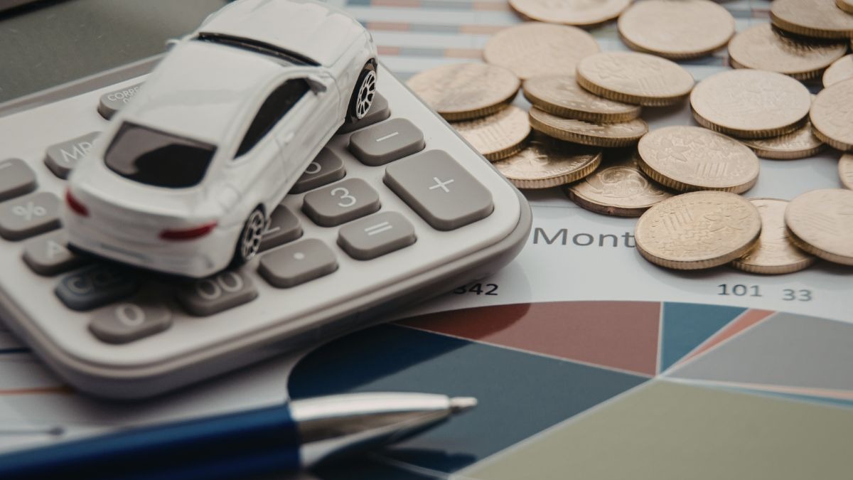 Um carro de brinquedo branco sobre uma calculadora, moedas e um documento financeiro.