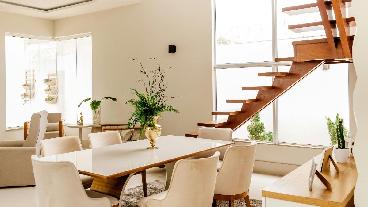 Sala de jantar moderna com mesa, cadeiras, plantas e escada de madeira iluminada