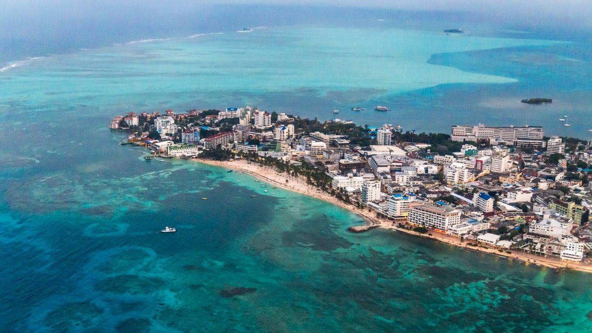 Praias caribenhas e águas cristalinas de San Andrés, na Colômbia, um destino ainda mais convidativo com a valorização do real. Vista aérea de cidade costeira com praia de areia branca, edifícios, mar azul e barcos.