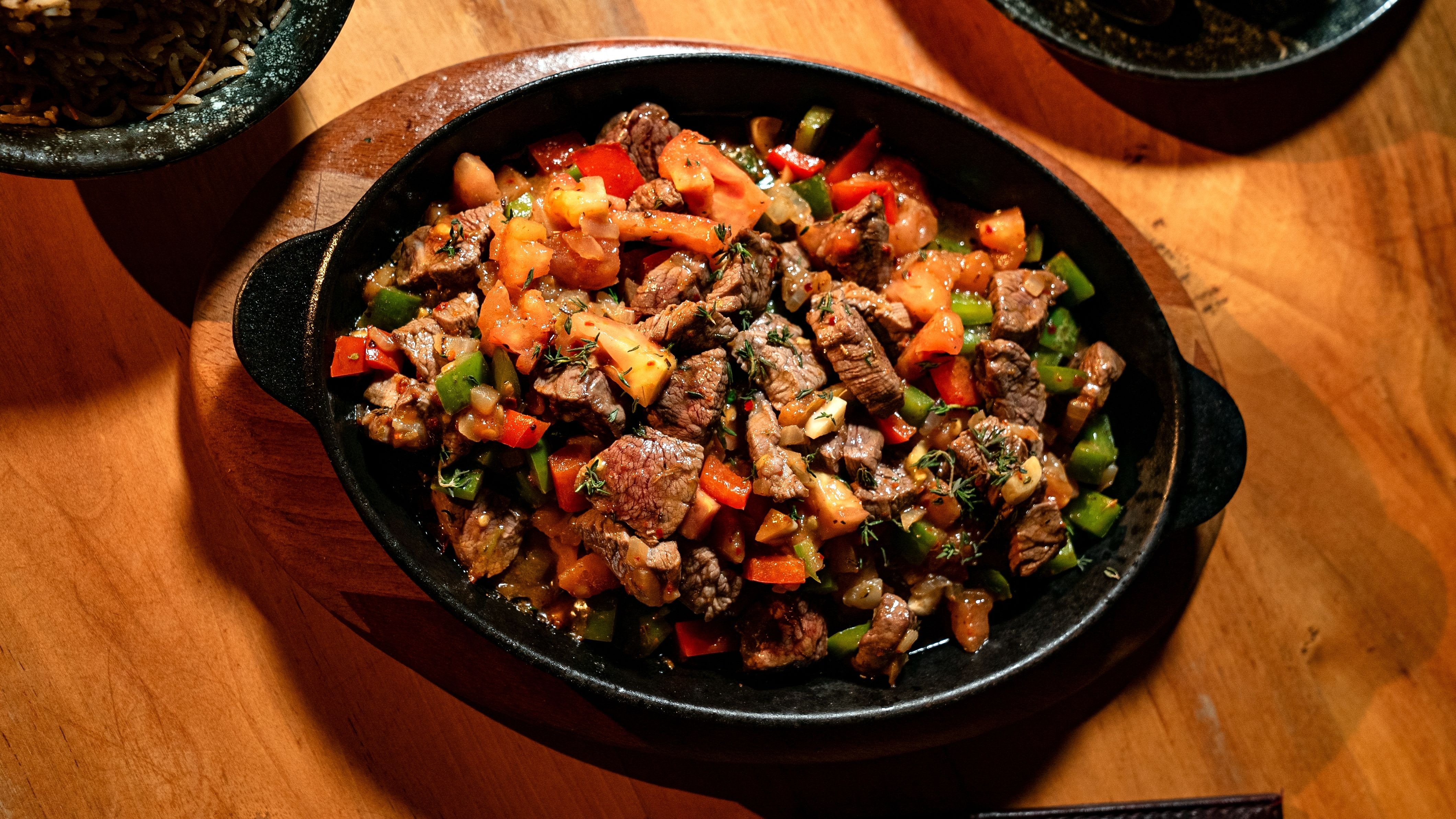 O entrevero de pinhão é um prato robusto da culinária serrana do Paraná, com diferentes carnes e legumes refogados em panela de ferro. Carne cozida com pimentões coloridos, tomates e ervas frescas em uma panela preta.