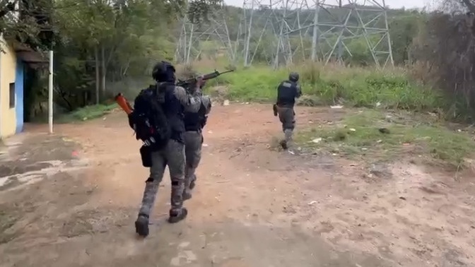 Agentes das tropas de elite da Polícia Militar em ação durante operação contra o crime organizado no Rio - Foto; Reprodução Três policiais militares em equipamento tático, um atira com fuzil, em área externa