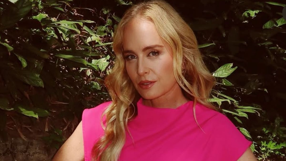 Aos 52 anos, a apresentadora Angélica compartilha sua rotina de bem-estar e hábitos matinais que garantem mais energia e disposição. Angélica, loira, em blusa rosa vibrante, posa com fundo de folhagens verdes.