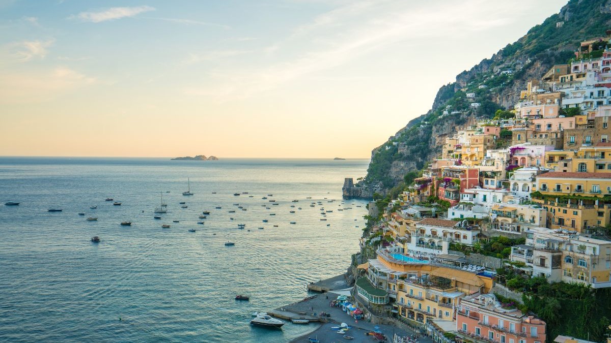 Positano, com suas casas em tons pastéis que descem em cascata até o Mar Tirreno, encanta os visitantes que buscam a beleza autêntica da Costa Amalfitana. Vista aérea de Positano, Itália, com casas coloridas na encosta e muitos barcos no mar.