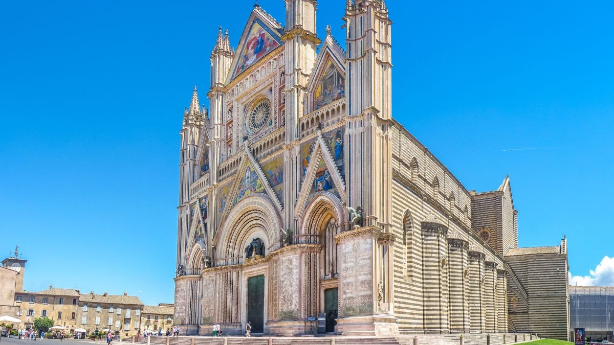 O Duomo de Orvieto, cartão-postal da cidade, ilustra o patrimônio histórico para quem busca nova vida na Itália. Grande catedral gótica com fachada ornamentada, mosaicos coloridos, rosácea, espigões e paredes listradas.