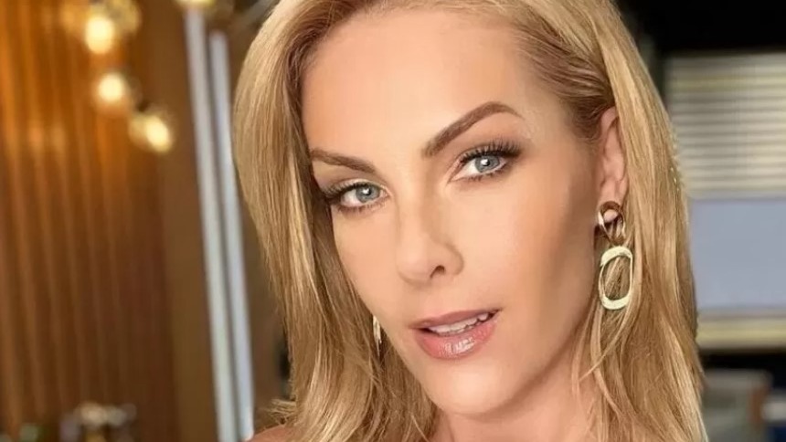 Ana Hickmann, cuja coragem redefiniu sua carreira após expor violência doméstica, como destacado na reportagem. Rosto de Ana Hickmann, mulher loira com maquiagem e brincos dourados, olhando para a frente.