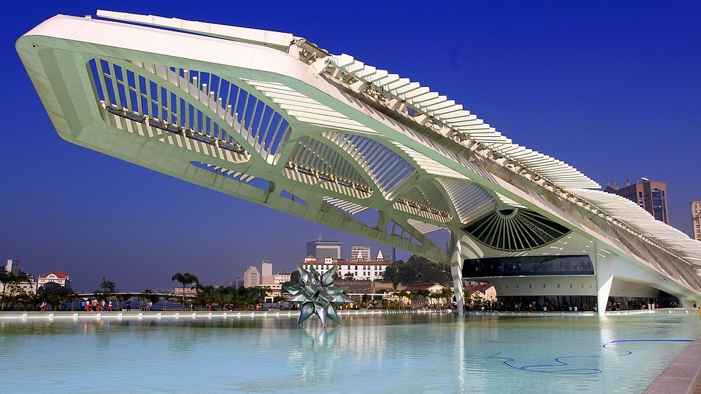 O Museu do Amanhã, um dos espaços da Semana de Arte do Rio, inaugura seu novo Jardim de Esculturas. Edifício branco futurista do Museu do Amanhã sobre espelho d'água, com skyline da cidade ao fundo
