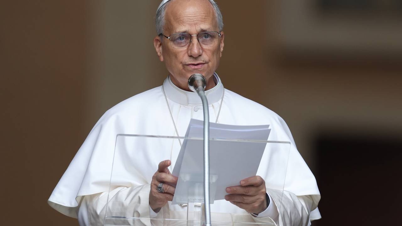 Papa Leão XIV faz pronunciamento público após o diagnóstico de nódulo pulmonar, antes de ser internado para cirurgia. Homem de óculos, vestes clericais brancas, falando ao microfone com papéis em pódio transparente