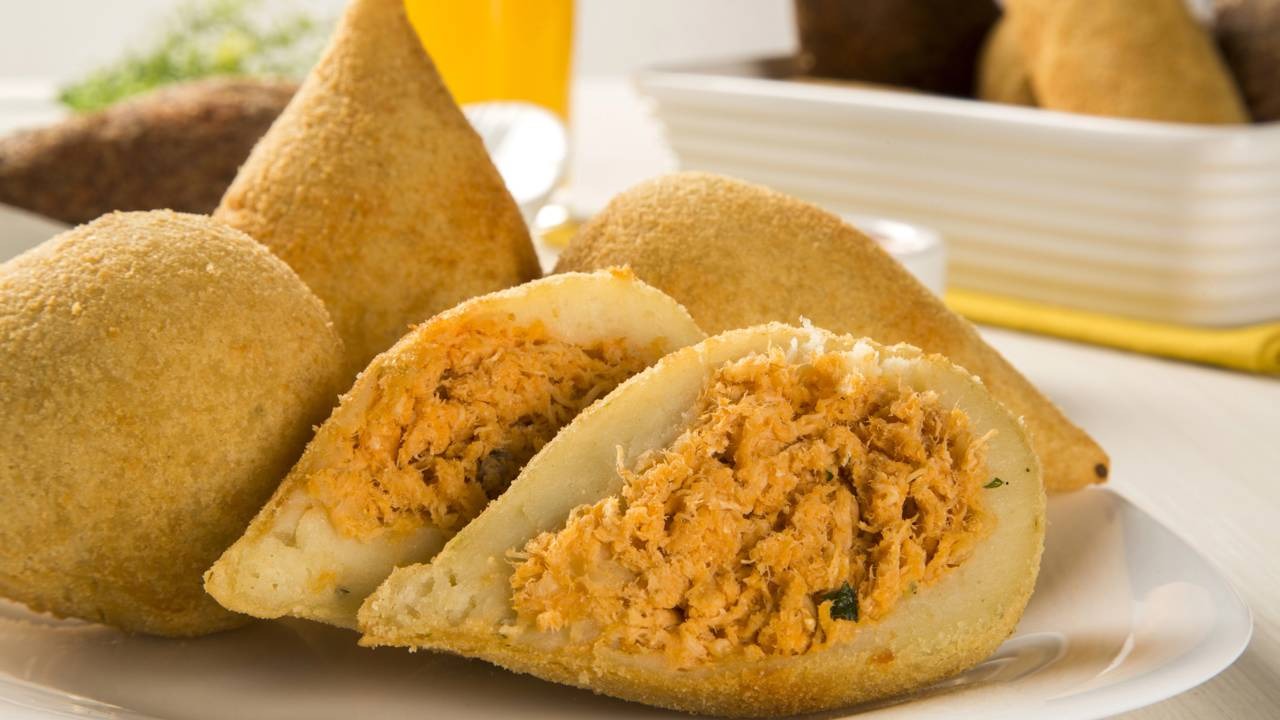A coxinha fit na Air Fryer oferece uma opção saborosa e saudável para quem busca um petisco sem culpa. Coxinhas douradas de frango empanadas, algumas cortadas ao meio mostrando o recheio desfiado