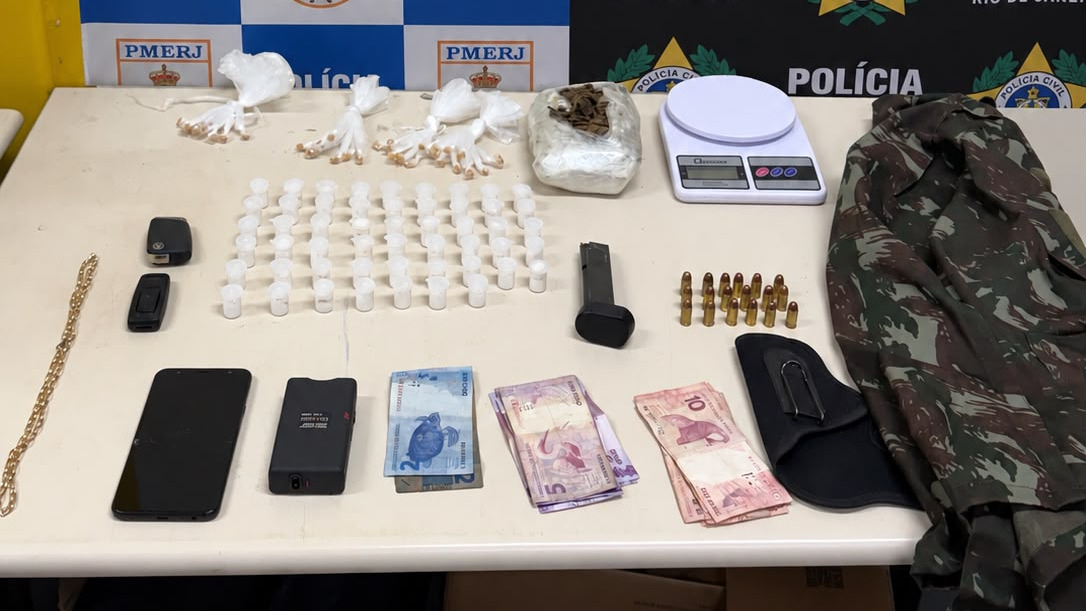 Material apreendido na operação conjunta das polícias Civil e Militar que resultou na prisão de dois homens e desmantelou ponto de tráfico de drogas - Foto; Reprodução Drogas, dinheiro, munições, carregador, balança, celulares, chaves e jaqueta camuflada em mesa