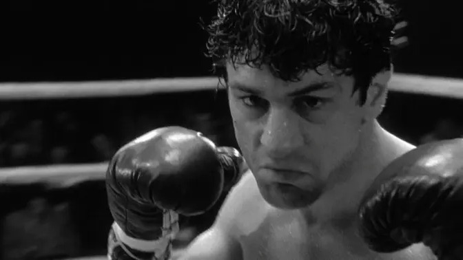 A intensa transformação de Robert De Niro como o boxeador Jake LaMotta em 'Touro Indomável', papel que lhe valeu um Oscar. Foto: Divulgação Robert De Niro como boxeador, suado, usando luvas de boxe, em imagem preto e branco.