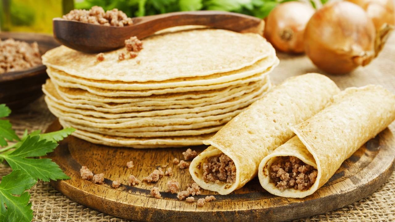 A receita de panqueca de carne moída garante um prato que sustenta, é prático de fazer e agrada a todos os paladares. Panquecas, algumas recheadas com carne moída, em tábua de madeira com cebolas e salsa