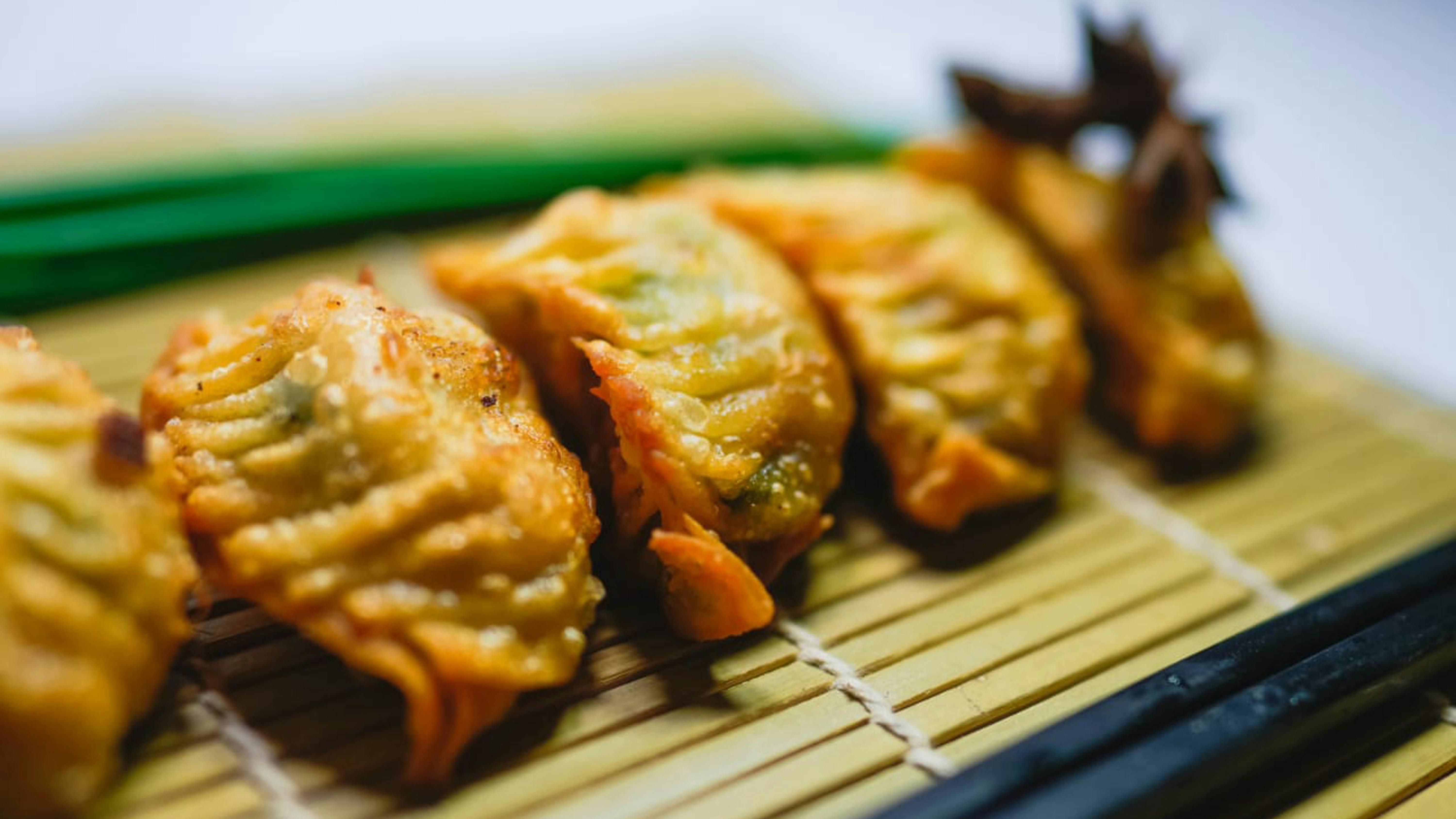 Gyoza dourados e crocantes em esteira de bambu, com hashi preto ao lado.