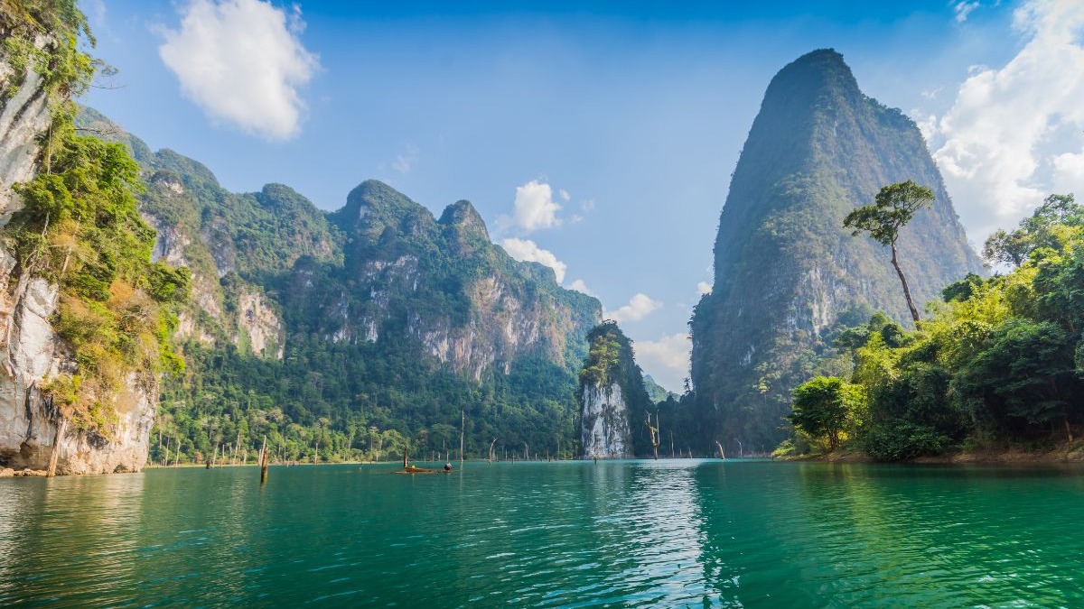Lagoa verde-esmeralda rodeada por montanhas rochosas e vegeta&ccedil;&atilde;o exuberante, com pequenas embarca&ccedil;&otilde;es e troncos.