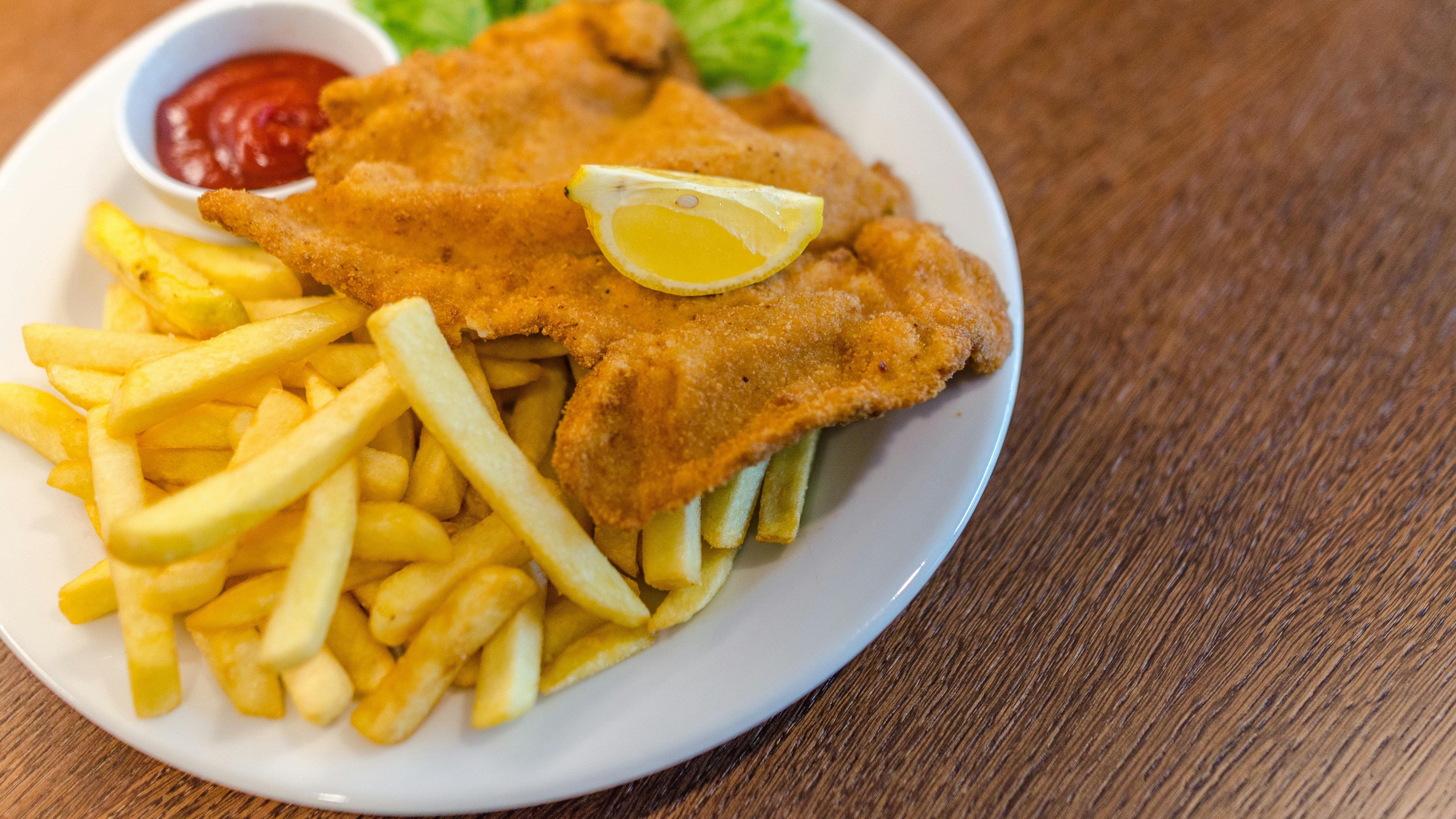 Prato branco com dois peda&ccedil;os de comida empanada frita, batatas fritas, lim&atilde;o e ketchup.