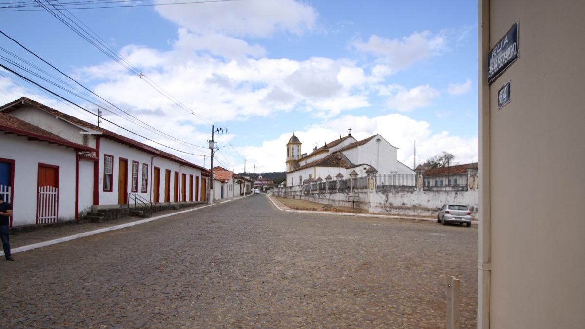 Rua de paralelep&iacute;pedos, casas brancas, igreja colonial e placa de rua 