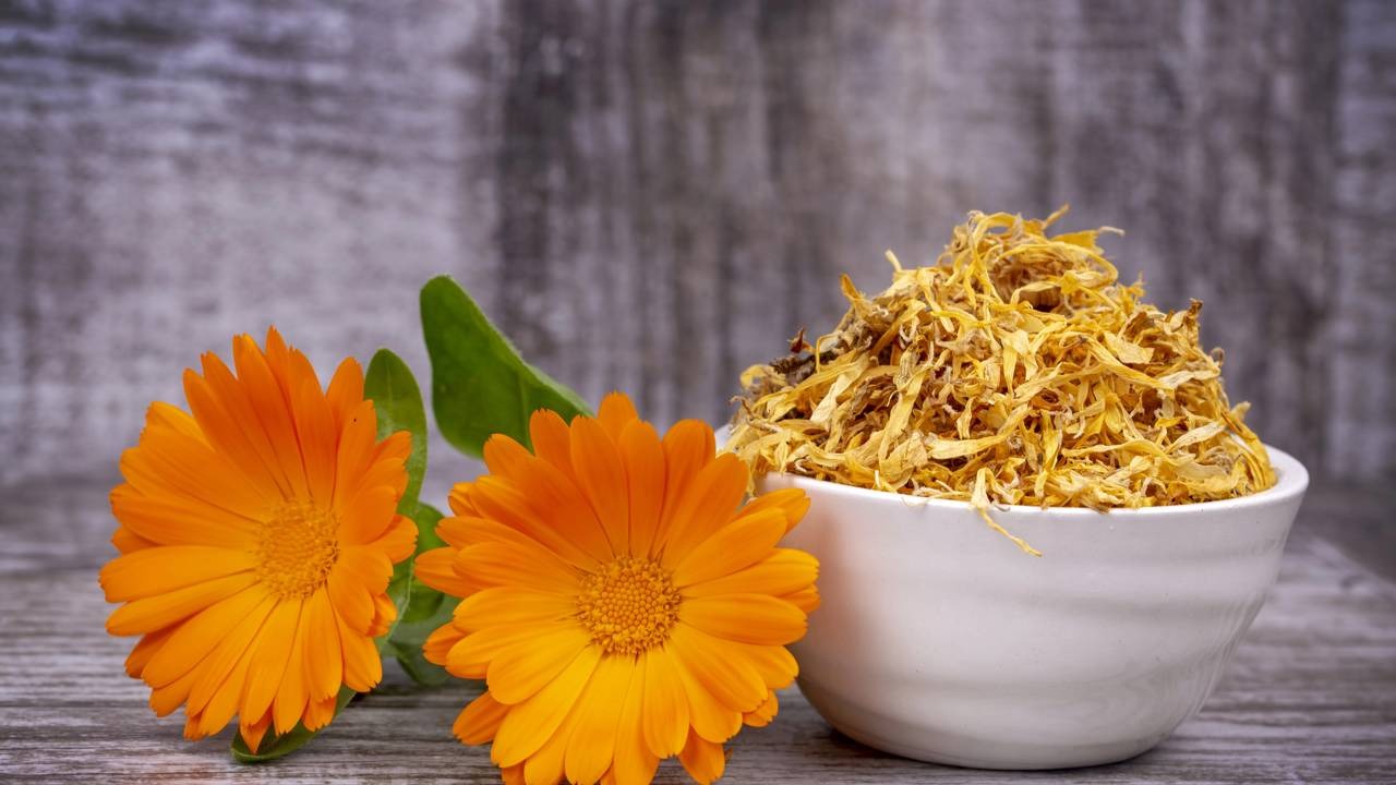 Flores de calêndula frescas e secas em uma tigela sobre uma superfície de madeira.