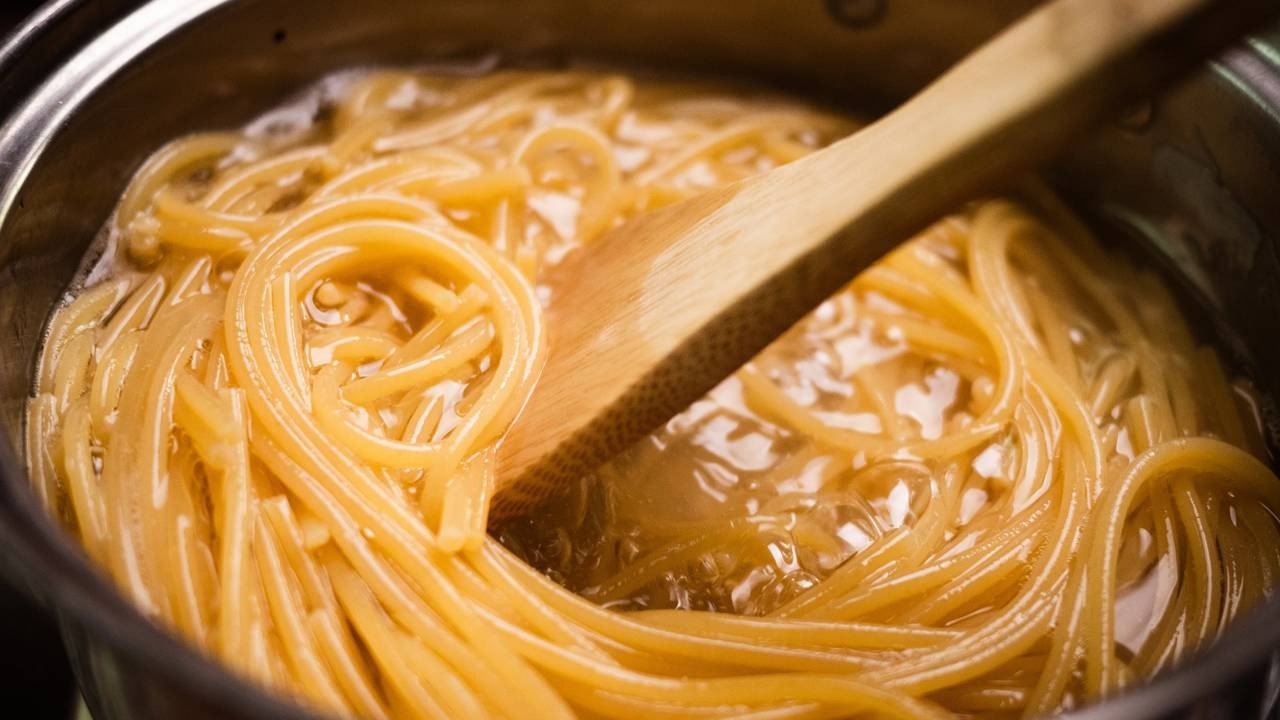 O cozimento da massa em água é a primeira etapa para atingir a textura al dente e absorver os molhos, conforme recomendam chefs. Spaghetti sendo cozido em panela com água fervente e mexido com uma colher de madeira