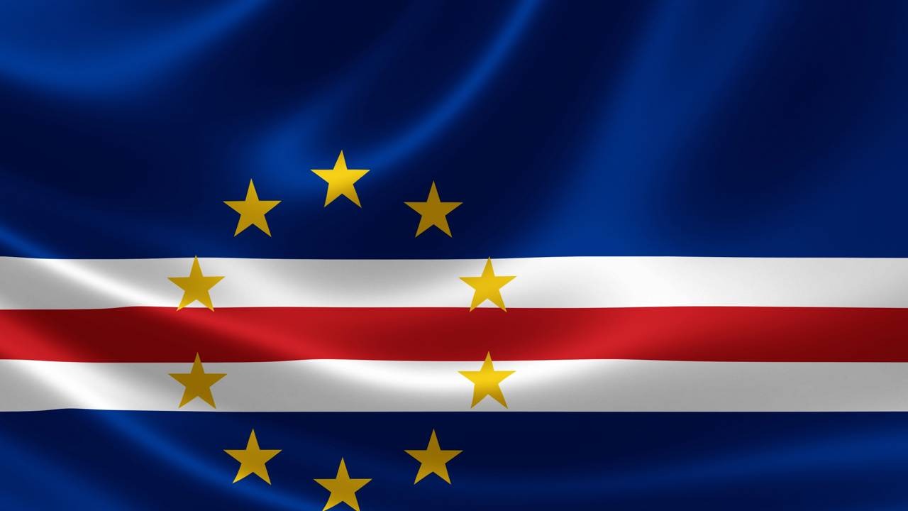 A bandeira de Cabo Verde, nação que se destacou na Copa do Mundo e é tema central desta reportagem sobre sua cultura e geografia. Bandeira de Cabo Verde ondulando, azul, com listras brancas, vermelha e dez estrelas amarelas.