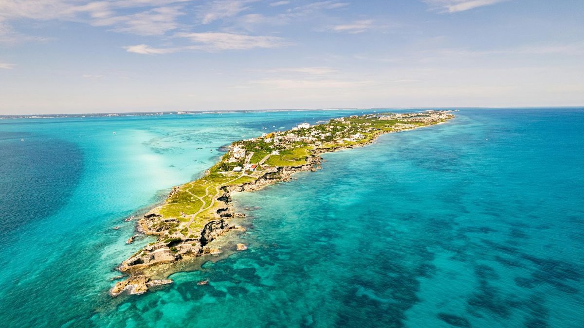 Vista a&eacute;rea de ilha tropical com casas, costa rochosa e mar azul-turquesa.