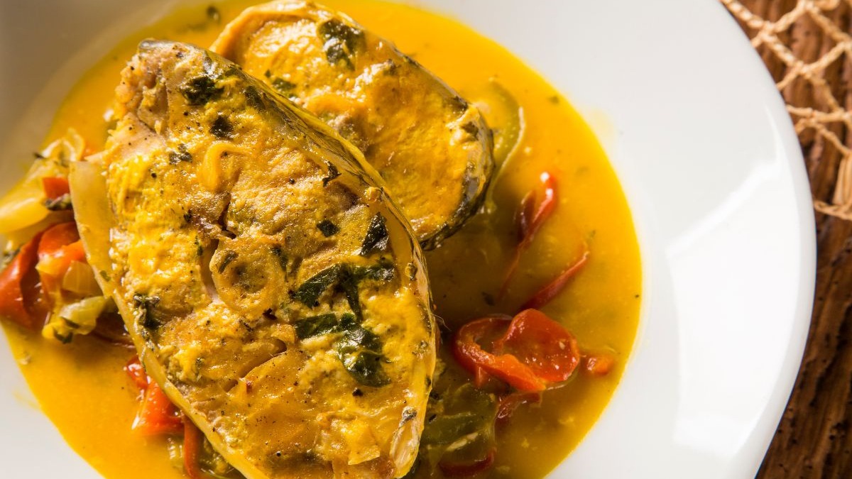 Um dos destaques da culinária de Mato Grosso do Sul, o peixe de rio em molho é um prato saboroso e autêntico do Pantanal. Dois pedaços de peixe em molho amarelo com pimentões vermelhos e ervas em prato branco.