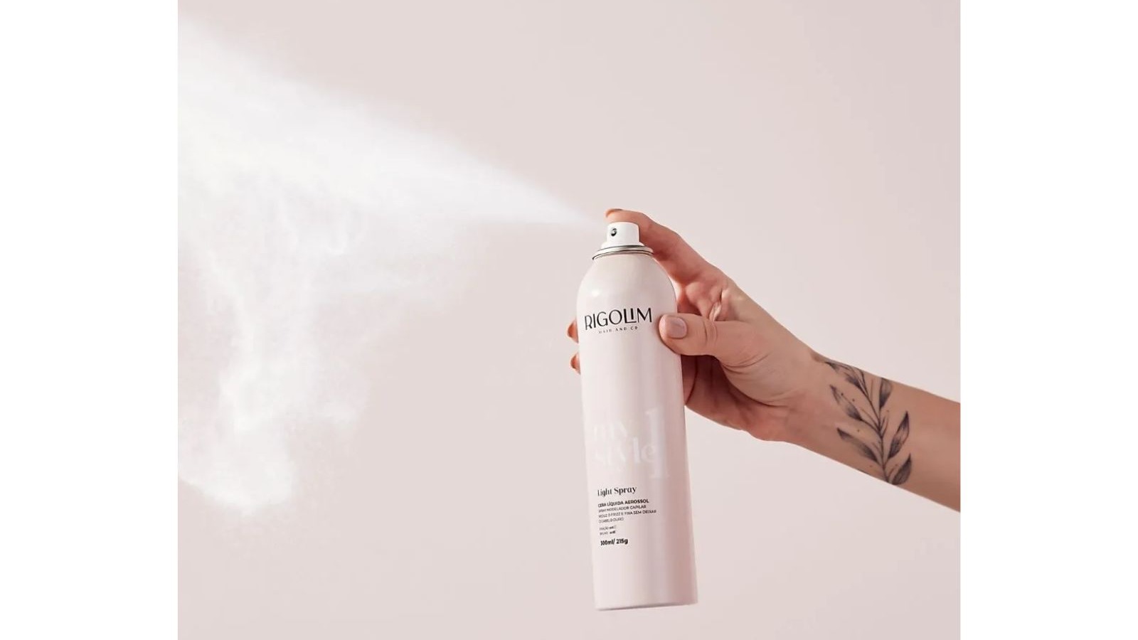 M&atilde;o feminina aplica Light Spray Rigolim, n&eacute;voa saindo do frasco rosa. Bra&ccedil;o tatuado